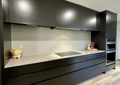 Modern kitchen with sleek black cabinets, light countertop, built-in stovetop, and double wall ovens.