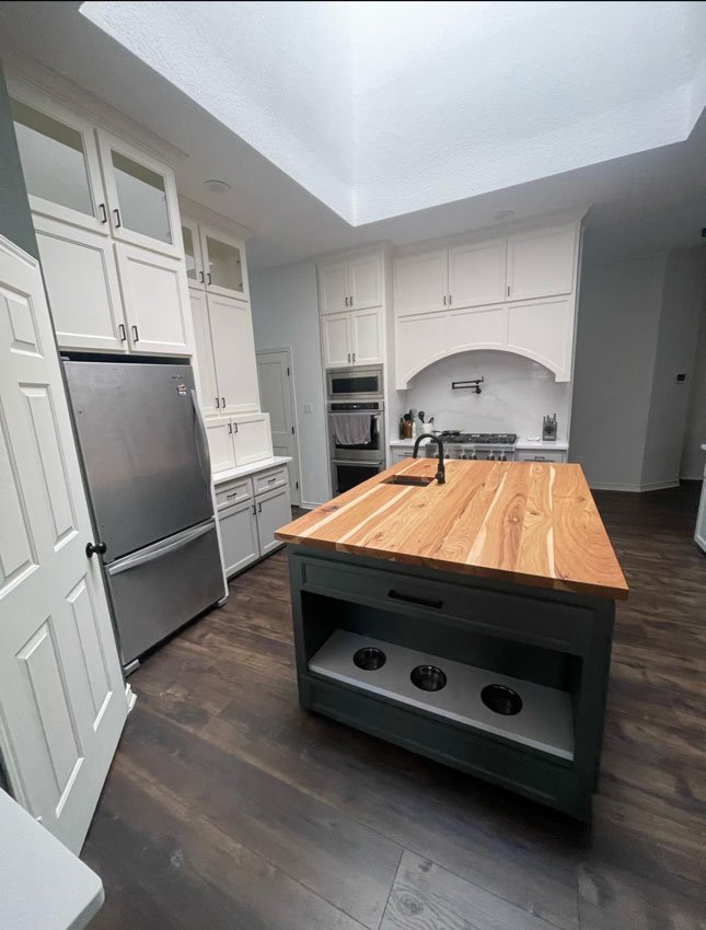 IMG_7325 Modern kitchen with wood island, built-in pet bowls, stainless appliances, white cabinets, and dark wood floor.