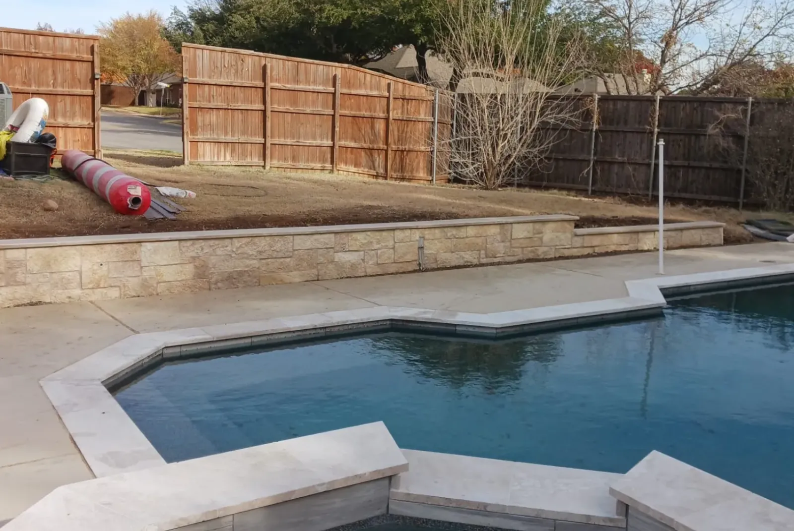 exterior-1 A backyard swimming pool with stone edging and wooden privacy fences in the background.