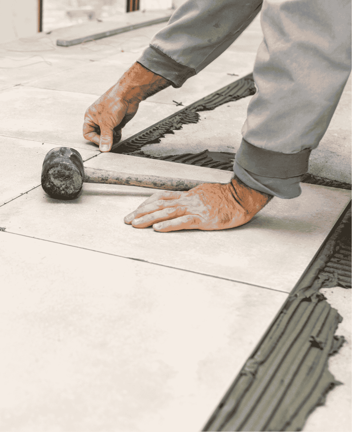 floor-2 A person installs floor tiles, using a rubber mallet and spacers to position and secure the tiles in place.
