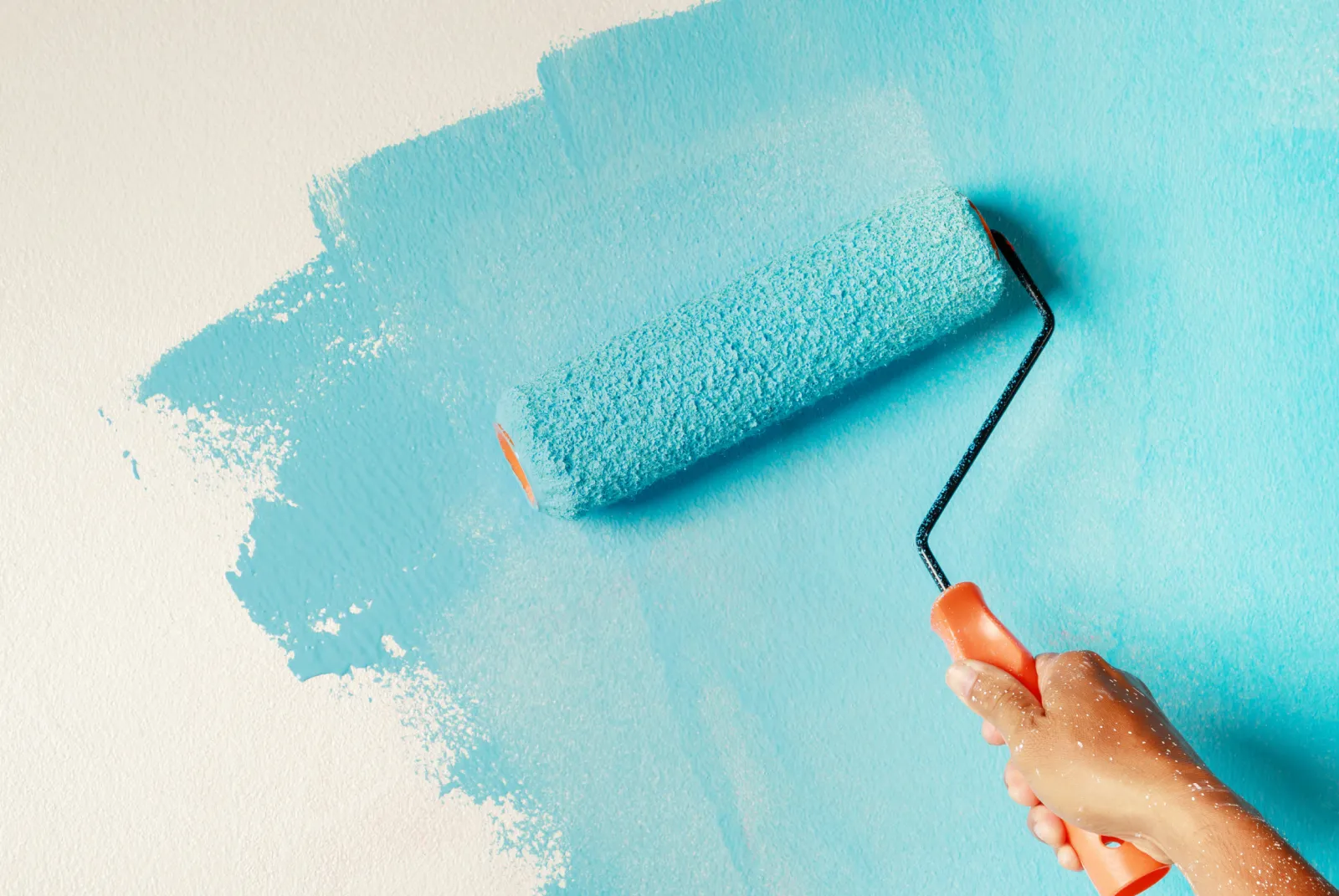 painting-1 A hand painting a white wall light blue with a paint roller.