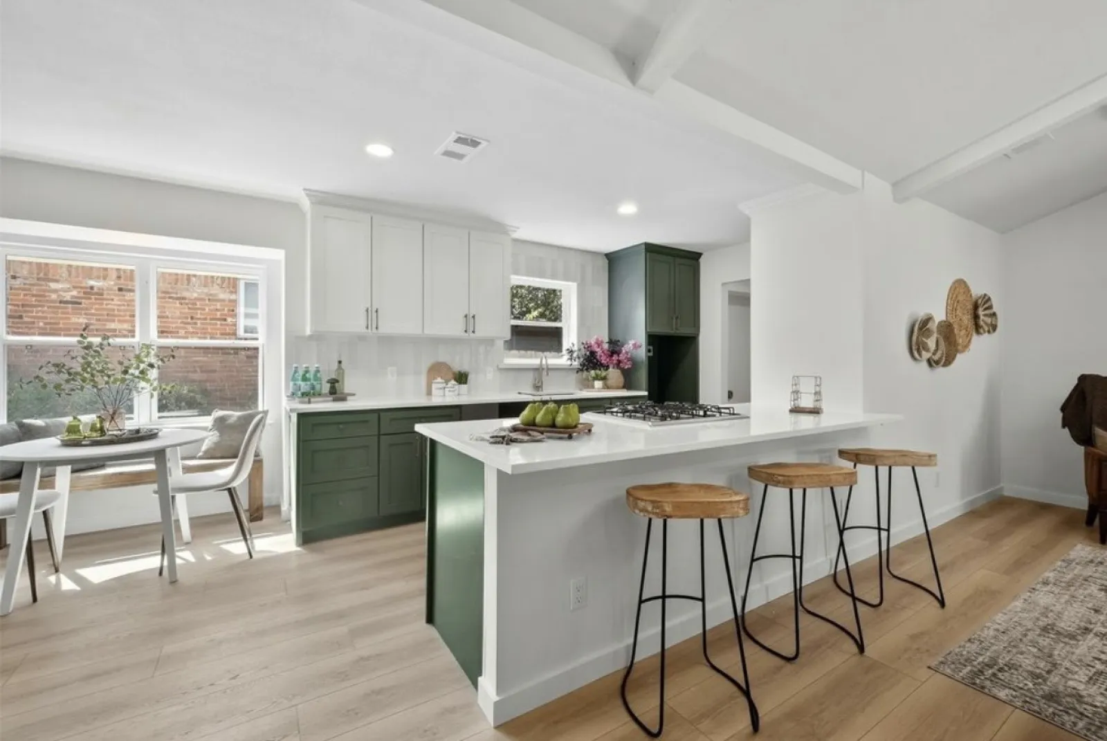 Bright modern kitchen with green and white cabinets, island seating, and a dining area by large windows.