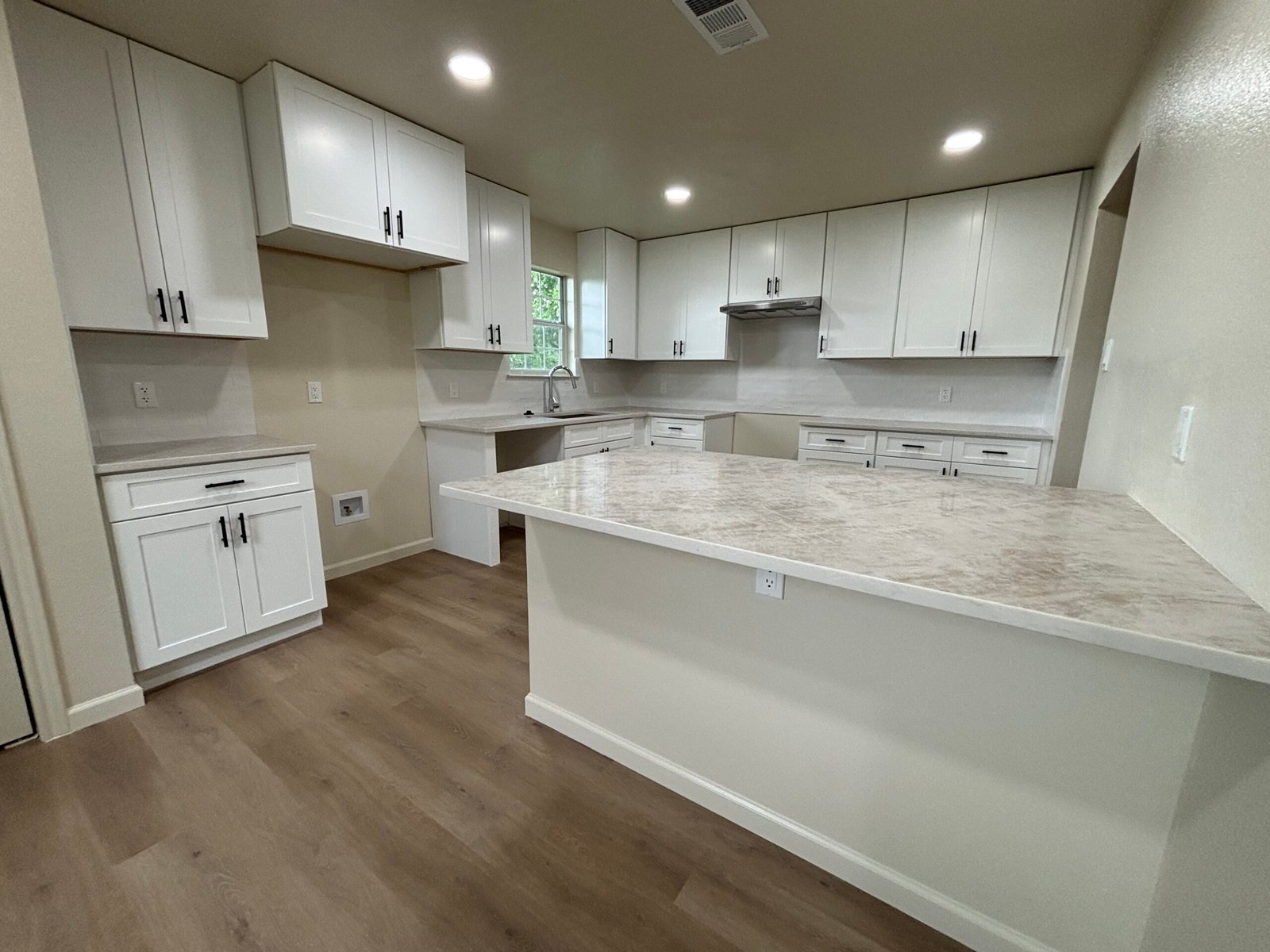 EE4F7232-F3F1-4AD4-9150-D698BD111AB4 Modern kitchen with white cabinets, marble island, four barstools, pendant lights, and wood accents.