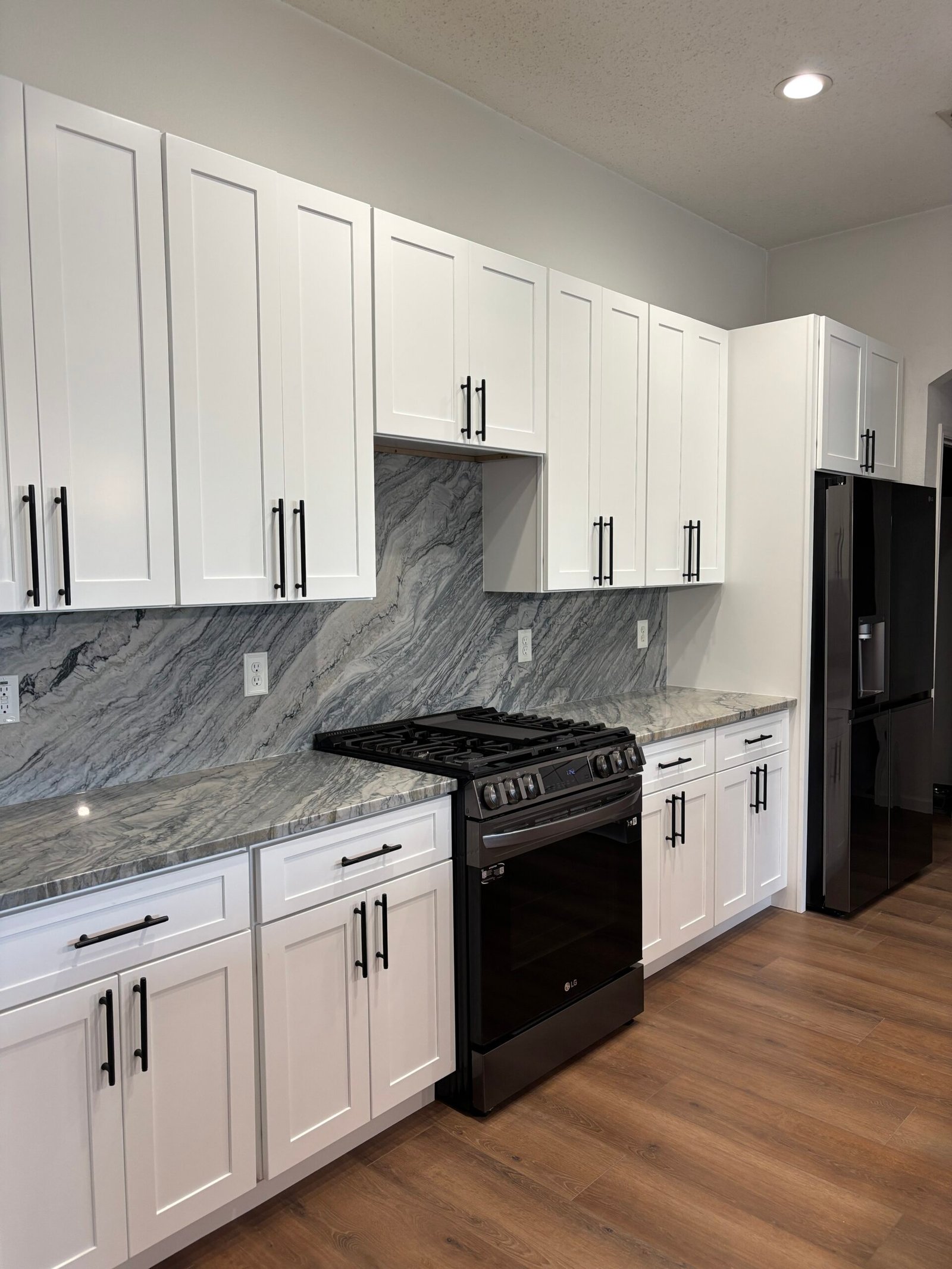 EE4F7232-F3F1-4AD4-9150-D698BD111AB4 Modern kitchen with white cabinets, marble island, four barstools, pendant lights, and wood accents.