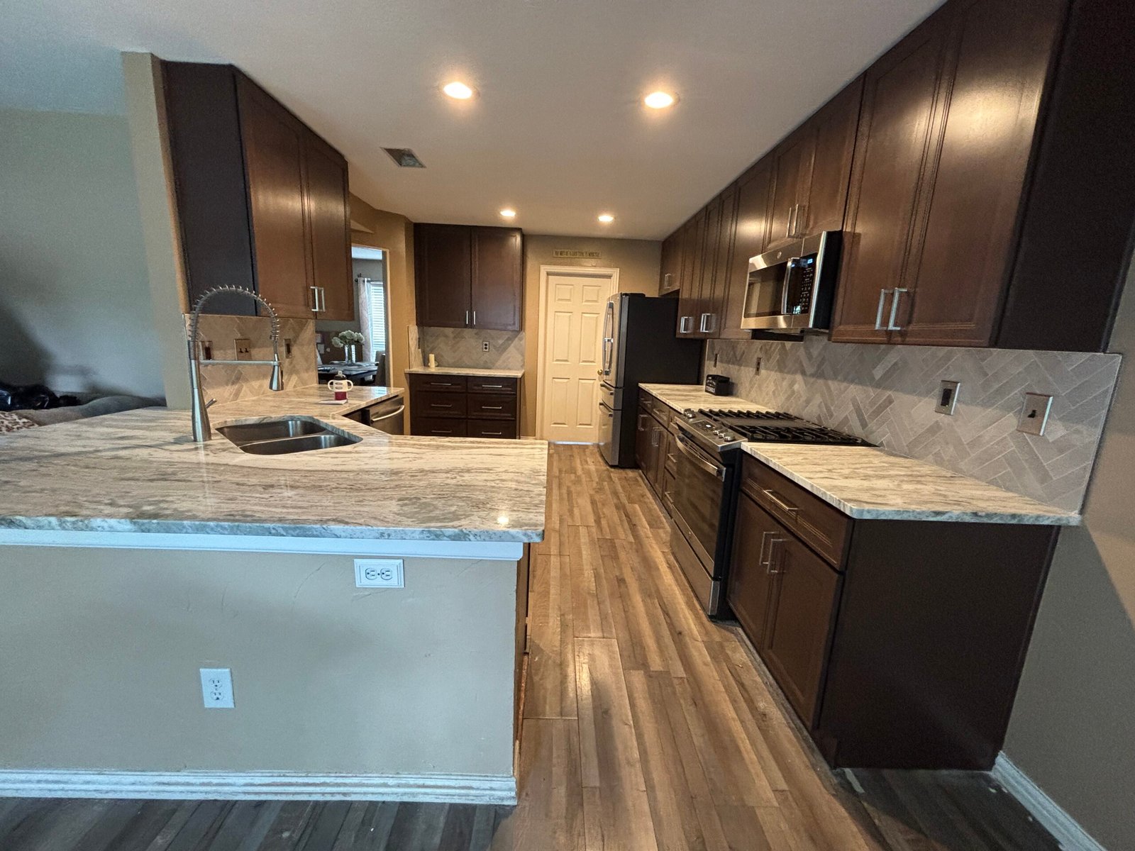 Modern kitchen with dark cabinets, marble countertops, tile backsplash, and wood flooring.