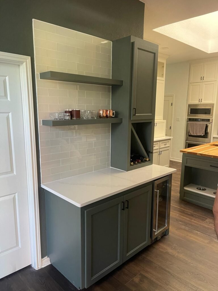 93FE9E07-1A2C-450B-8D72-0945068D5EF6 Modern kitchen with white cabinets, a large island, pendant lights, and wooden accents.
