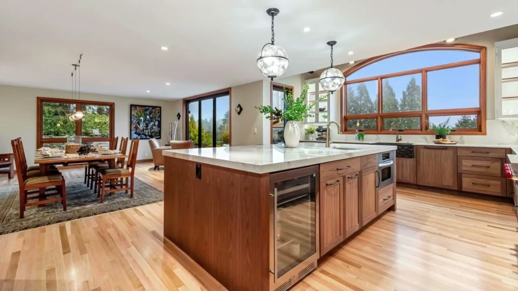 93FE9E07-1A2C-450B-8D72-0945068D5EF6 Modern kitchen with white cabinets, a large island, pendant lights, and wooden accents.