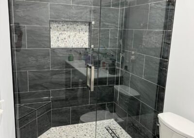 Walk-In Shower Remodel with Dark Tile, Pebble Floor, and Built-In Bench