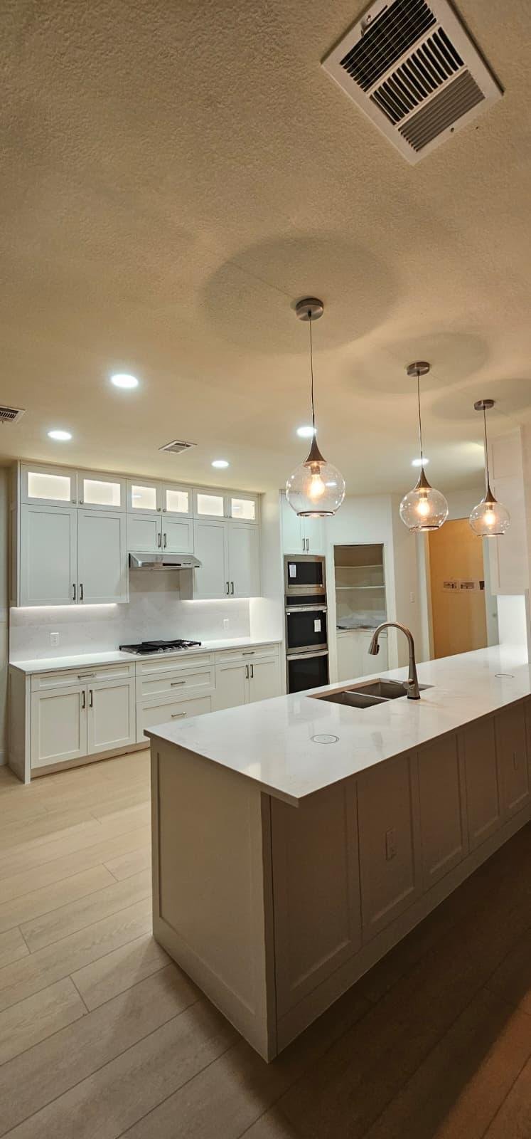 Modern kitchen with white cabinets, marble island, four barstools, pendant lights, and wood accents.